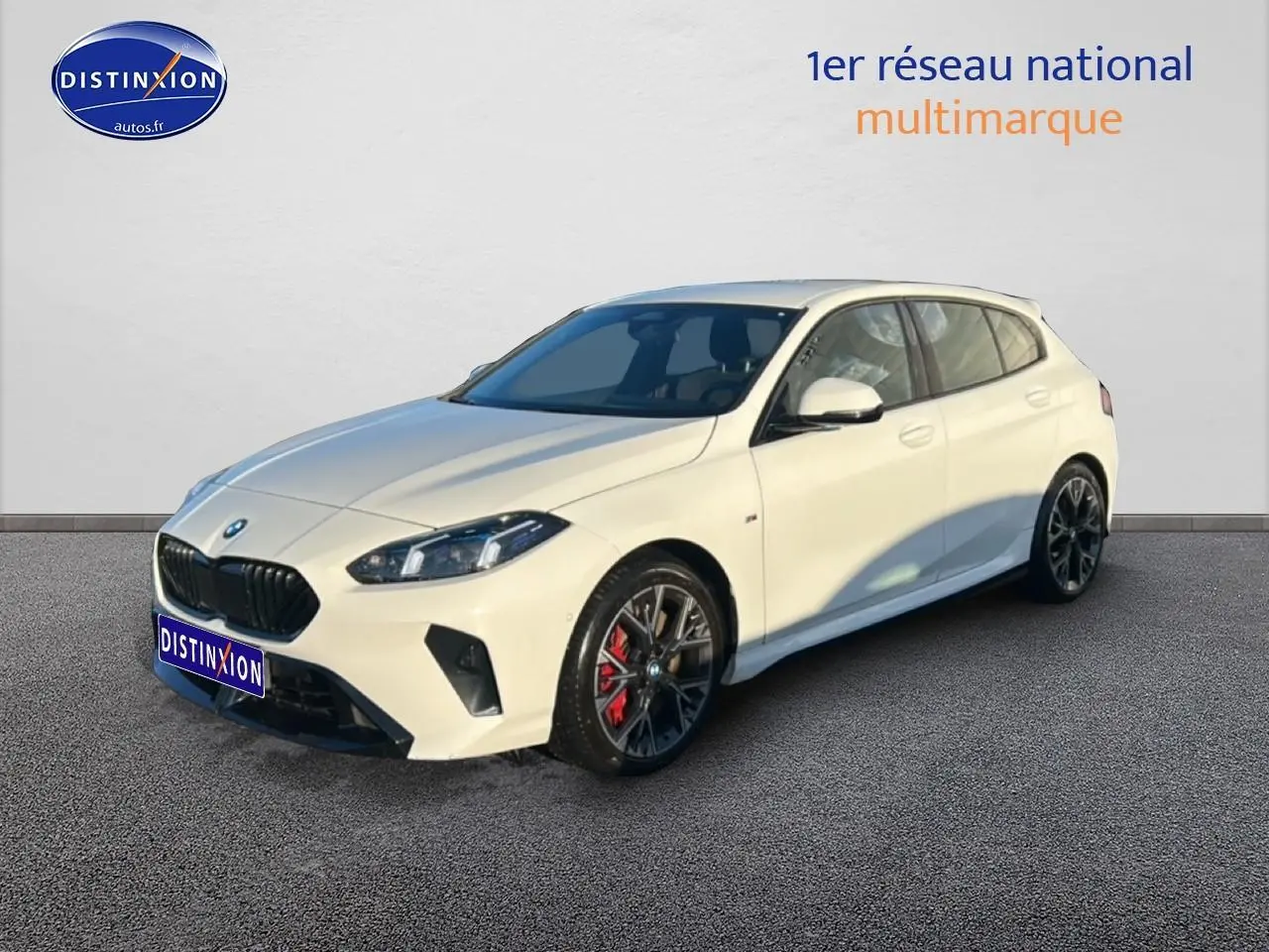 BMW Série 1 blanche alpin vue 3/4 avant droit, avec jantes 18 pouces bicolores et étriers rouges visibles.