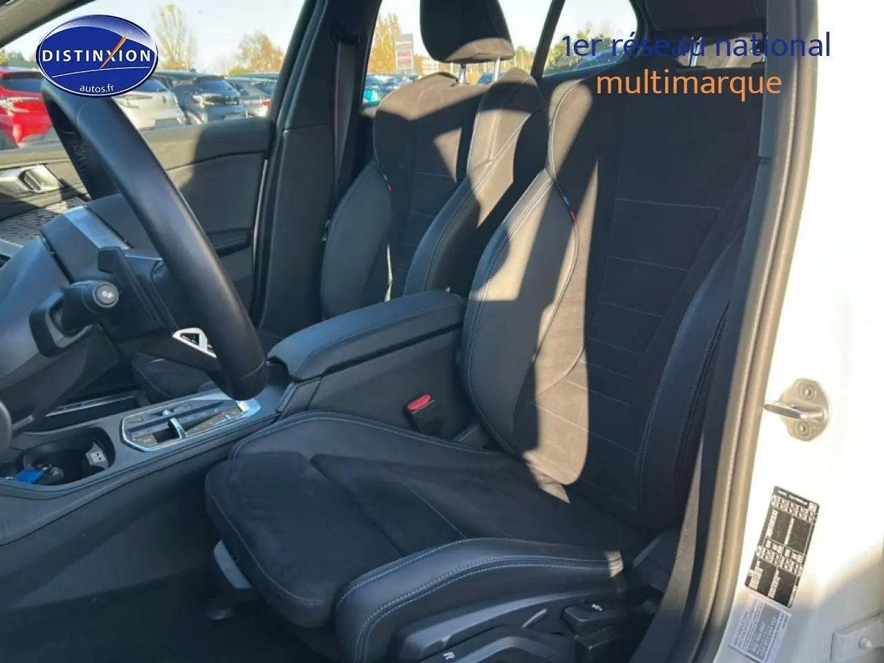 Vue intérieure côté conducteur de la BMW Série 1 blanche, sièges sport en alcantara noir avec coutures bleues.