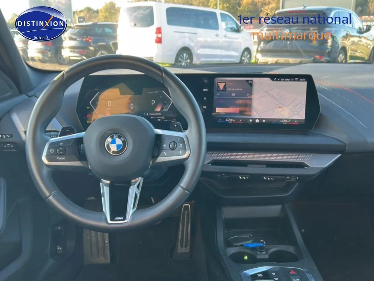 Vue intérieure avant de la BMW Série 1 blanche, volant M sport et écran tactile central avec navigation affichée.