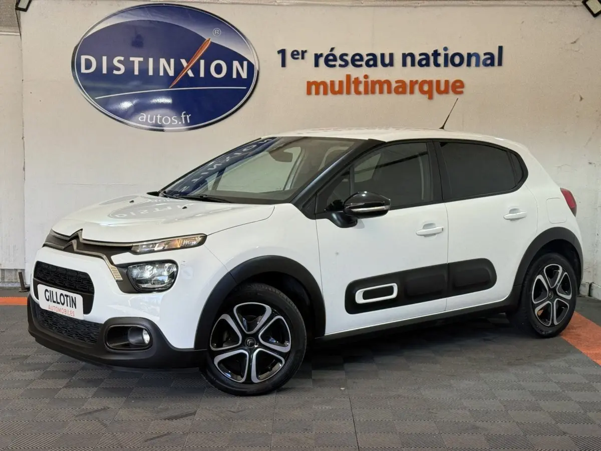 Citroën C3 blanche vue 3/4 avant droit, avec protections latérales noires et jantes stylisées bicolores.