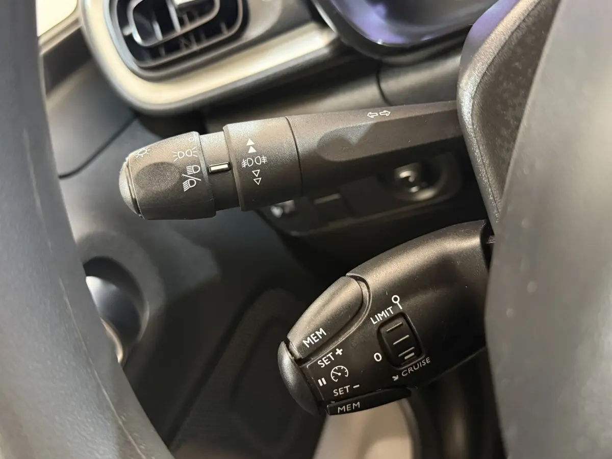Gros plan sur les commandes au volant noir du Citroën C3 blanc, mettant en valeur les boutons du régulateur de vitesse et des feux.