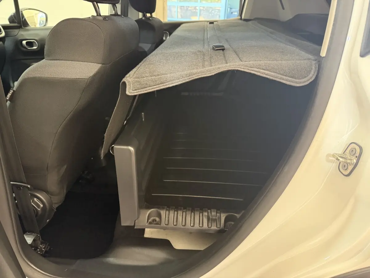 Vue intérieure côté droit du coffre ouvert d'une Citroën C3 blanche avec banquette arrière rabattue et cache-bagages déployé.