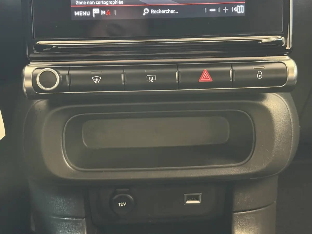 Vue rapprochée de la console centrale noire de la Citroën C3 blanche, avec commandes et prise 12V visible.