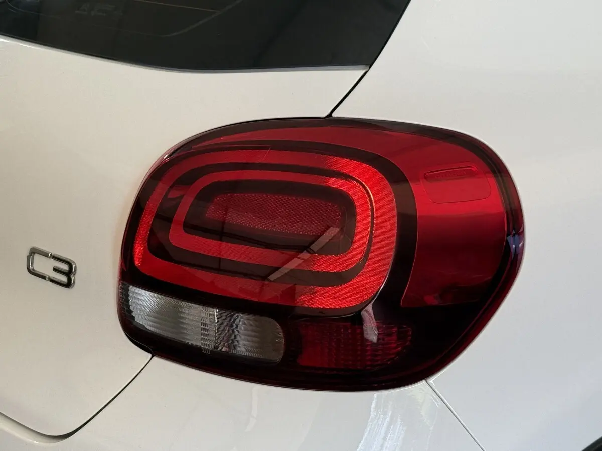 Gros plan sur le feu arrière droit rouge et blanc d'une Citroën C3 blanche, avec le logo C3 visible sur la carrosserie.