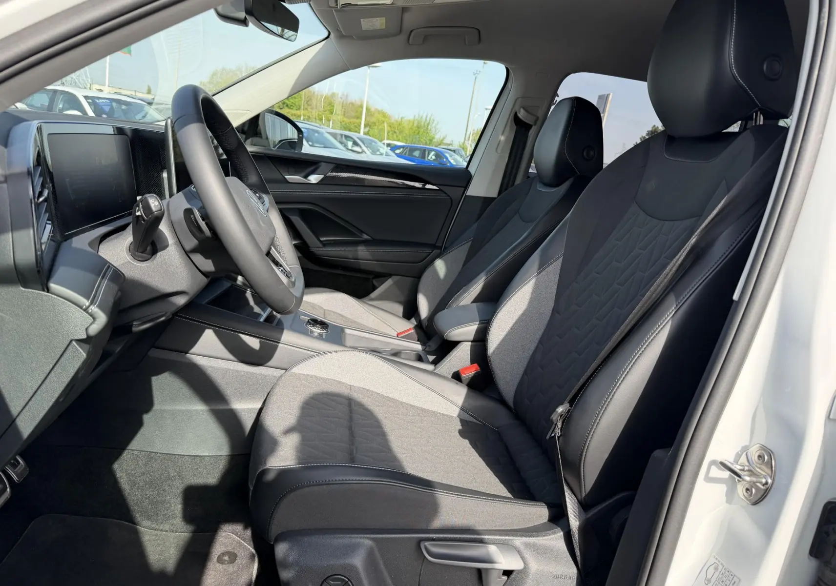 Vue intérieure côté conducteur du Volkswagen Tiguan blanc 2025, sièges tissu et cuir noirs avec console centrale moderne.