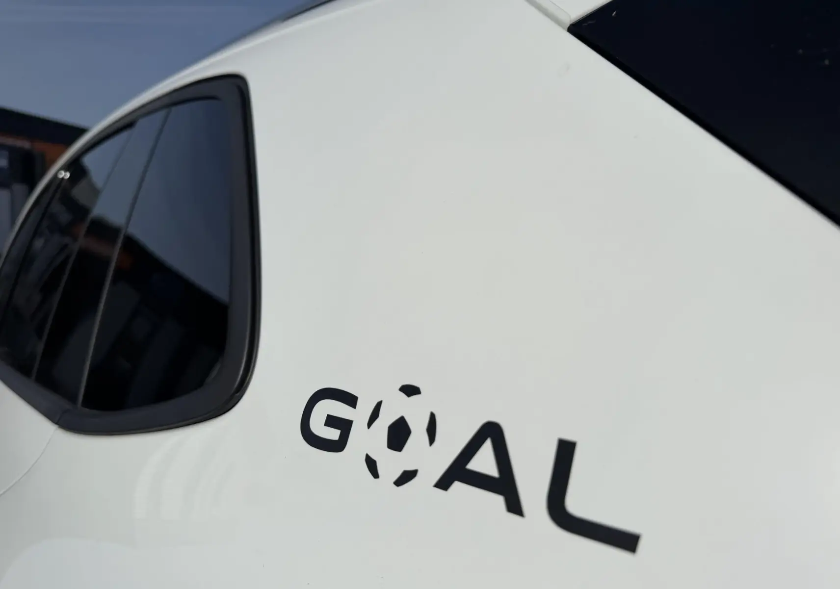 Gros plan sur la partie arrière gauche blanche du Volkswagen Tiguan avec l’inscription noire "GOAL" stylisée ballon de foot.