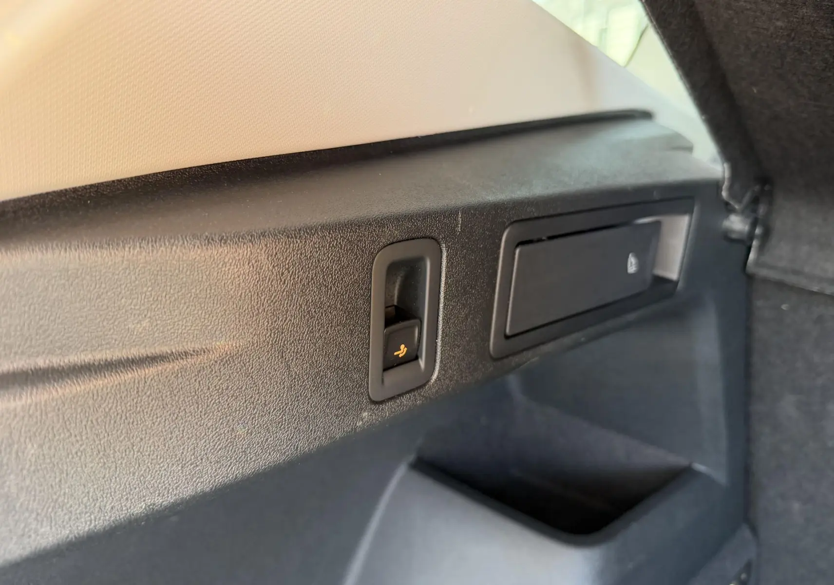 Gros plan sur la commande de rabattement des sièges dans le coffre du Volkswagen Tiguan blanc, intérieur noir.