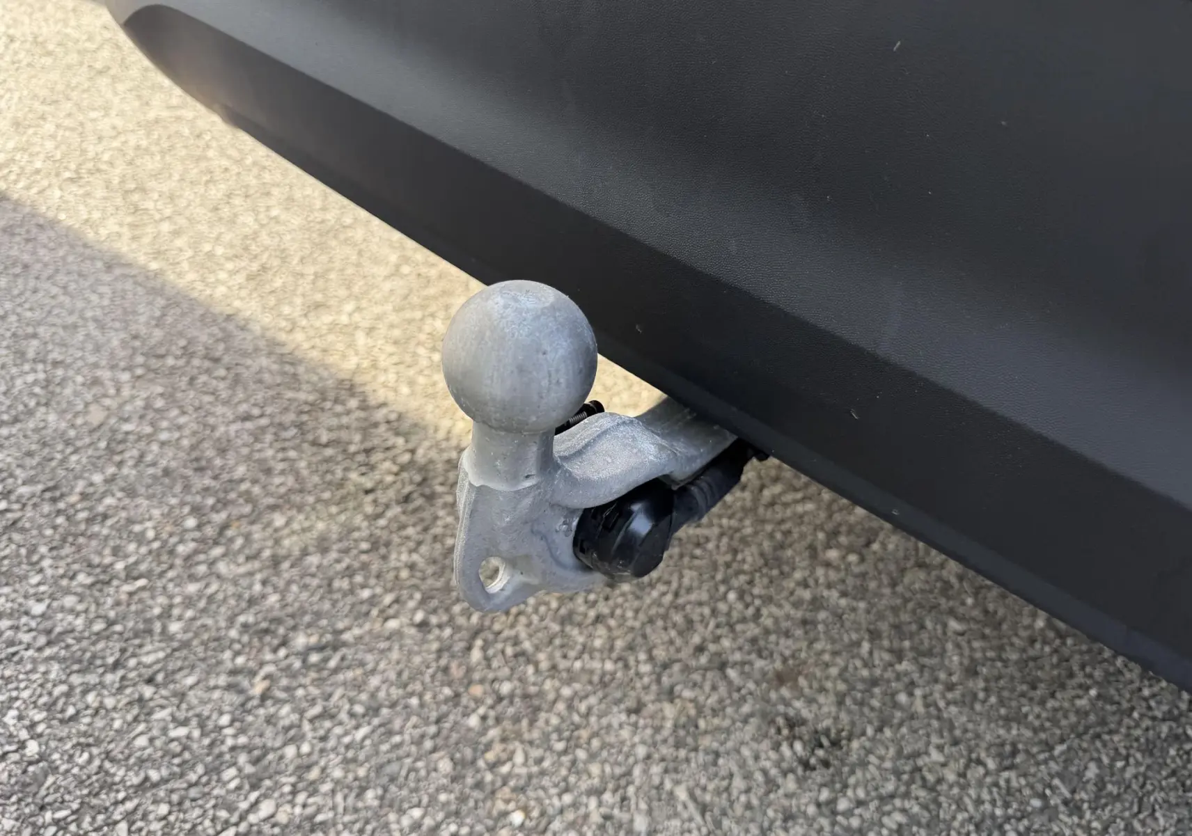 Gros plan sur l'attelage rabattable gris fixé sous le pare-chocs arrière noir du Volkswagen Tiguan blanc.