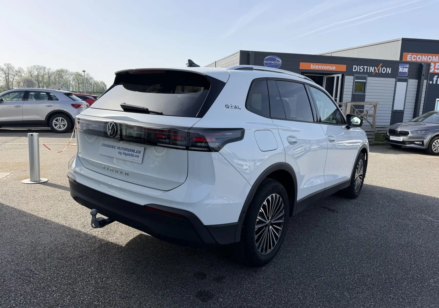 Vue 3/4 arrière droite d’un Volkswagen Tiguan blanc avec attelage et jantes alliage noir brillant, stationné en extérieur.