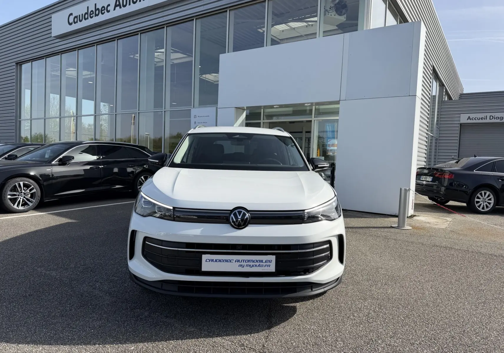 Volkswagen Tiguan blanc vu de face, avec calandre noire et logo VW centré devant un showroom.