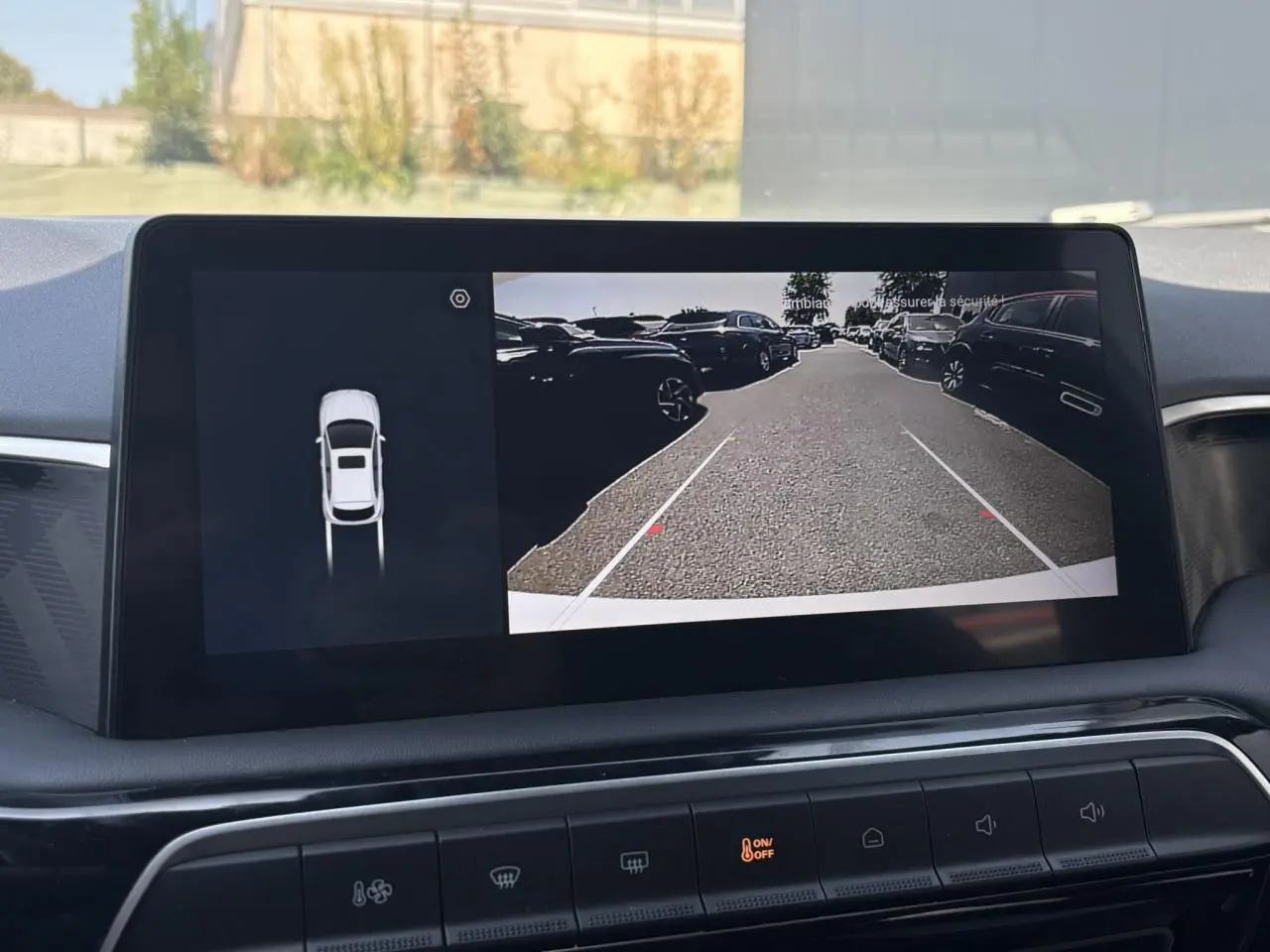 Écran central tactile montrant la caméra de recul du MG3 blanc Dover, avec vue arrière sur un parking extérieur.