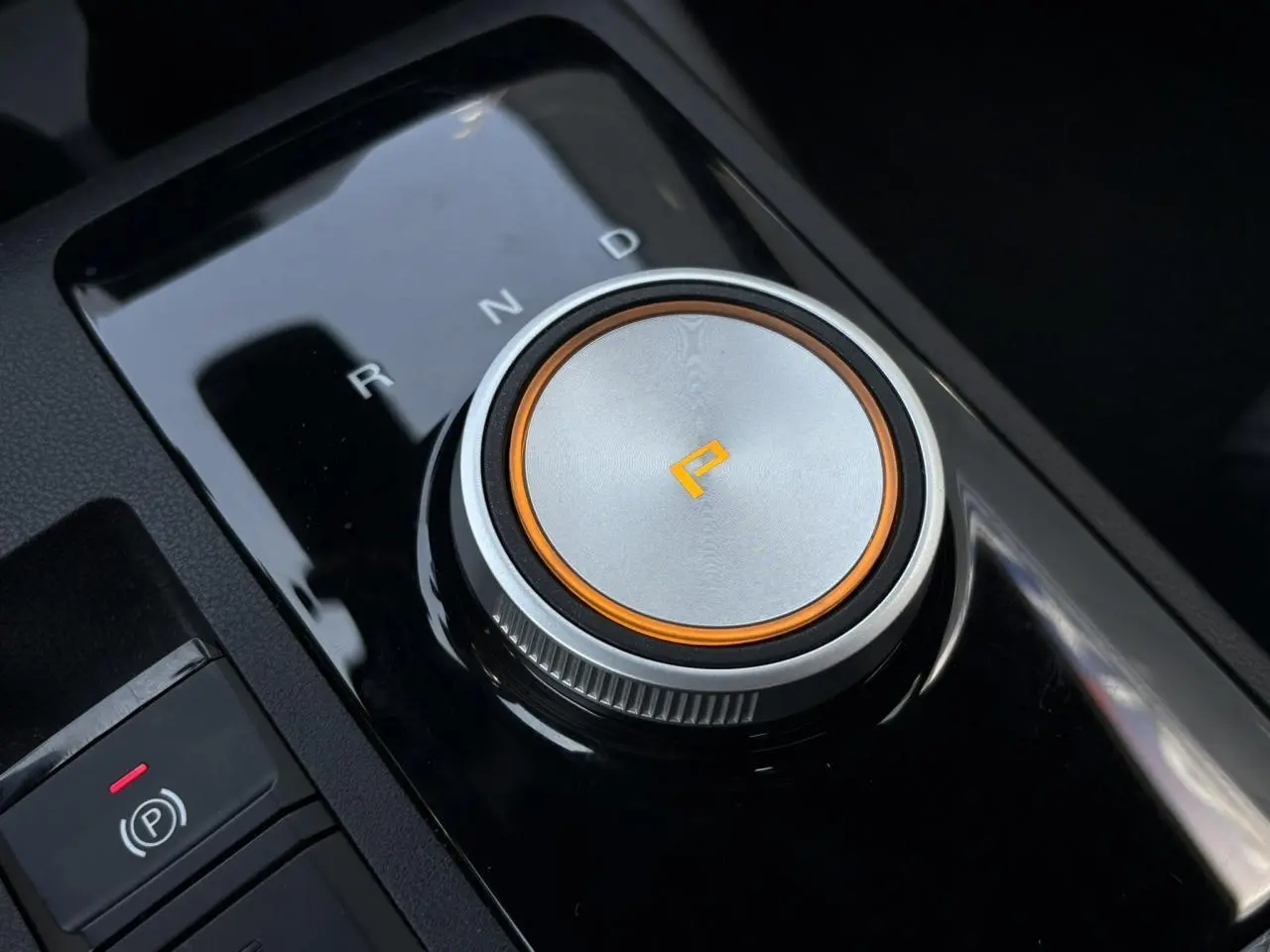 Gros plan sur la molette de sélection de boîte automatique argentée avec éclairage orange dans l’habitacle noir du MG3 blanc.