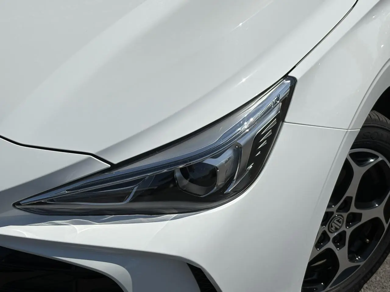 Gros plan sur le phare avant droit et la roue alliage 16'' d’un MG3 blanc Dover 2025.