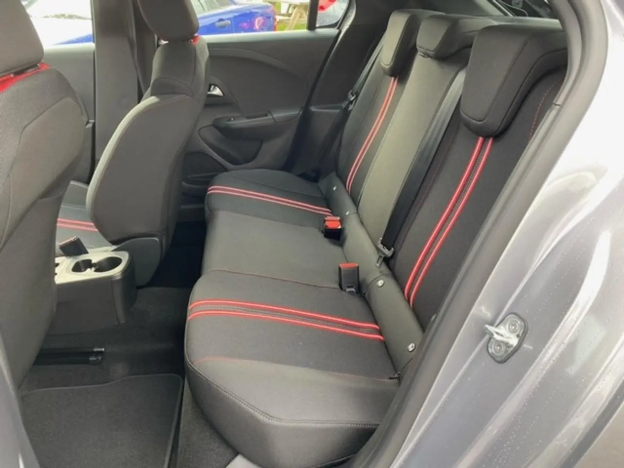 Vue côté droit de l'habitacle arrière de l'Opel Corsa 2022 avec sellerie tissu noire et bandes rouges contrastantes.