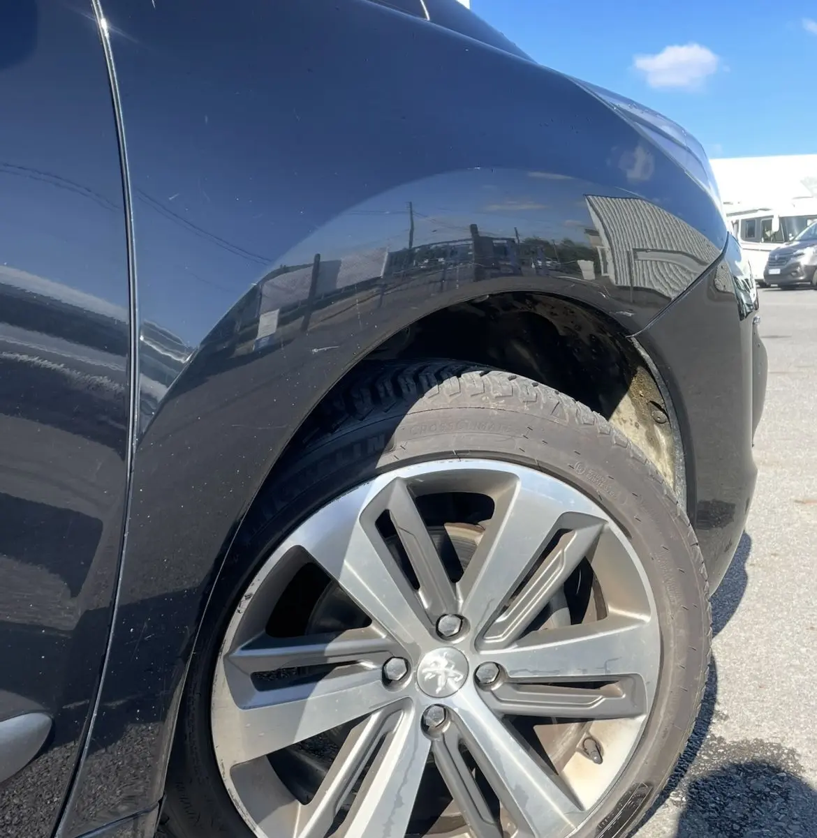 Gros plan sur la roue avant droite d’un Peugeot 3008 noir, mettant en valeur la jante alliage au soleil.