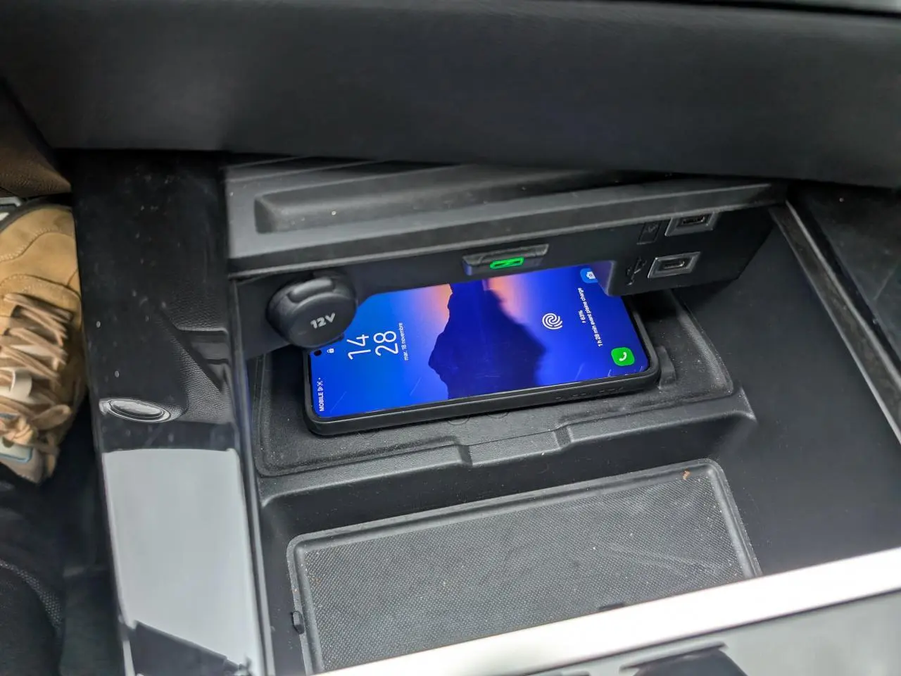 Gros plan sur la console centrale de l’Opel Astra 2024 avec smartphone en charge sans fil et prise 12V visible.