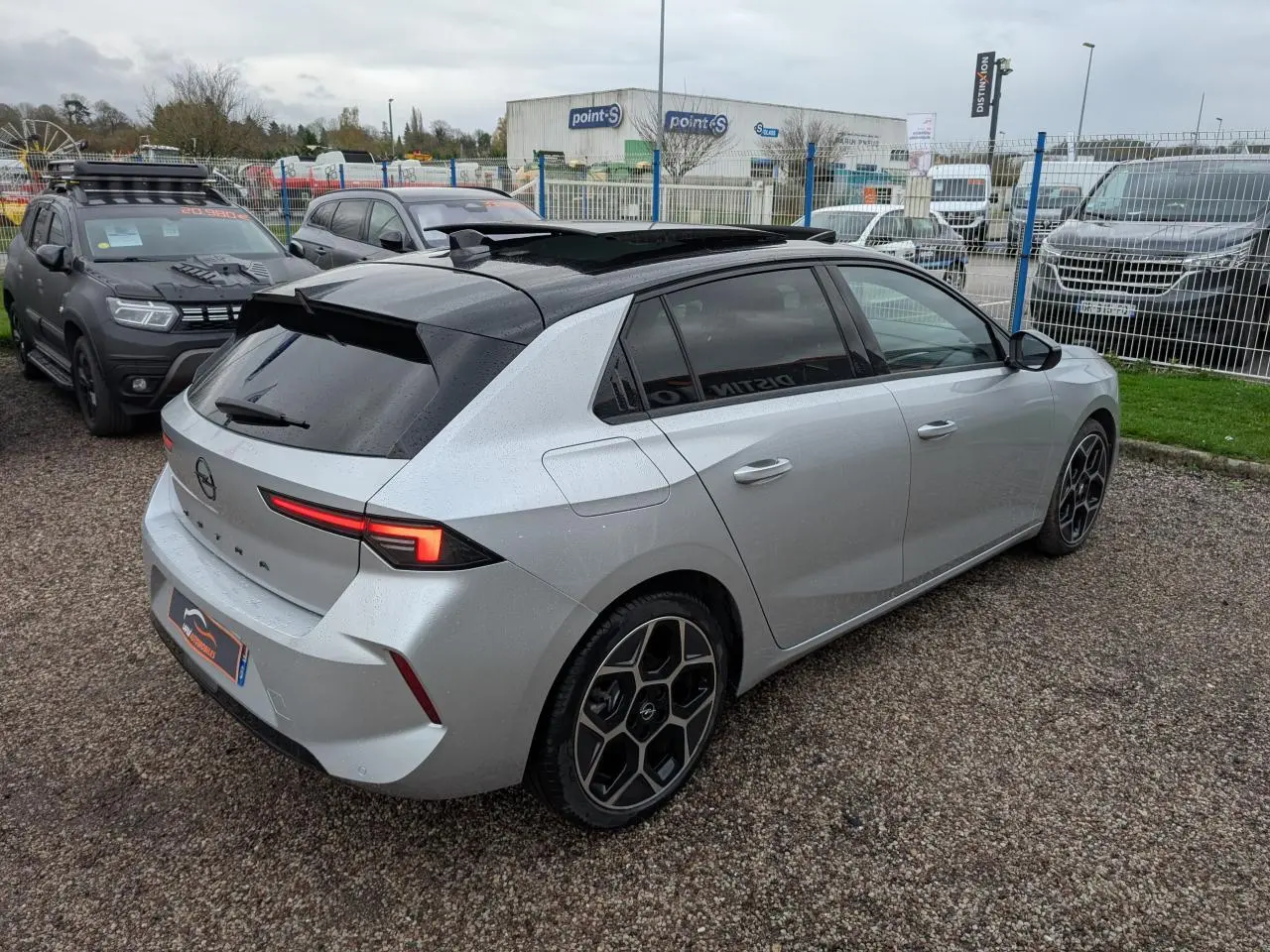 Opel Astra 2024 gris métallisé vue 3/4 arrière droit avec toit noir et jantes alliage 18 pouces pentagonales.
