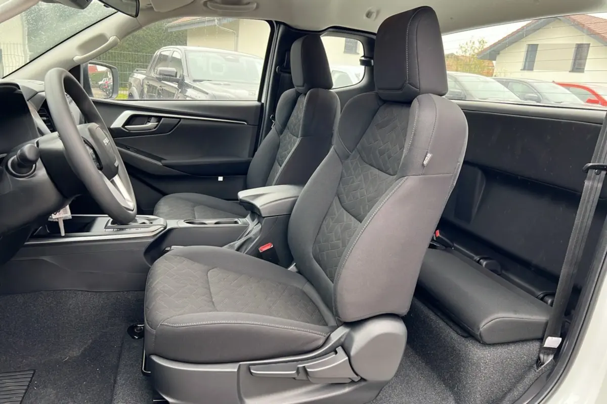 Vue intérieure côté gauche du pick-up Isuzu D-MAX 2026 Splash White, montrant les sièges avant en tissu gris et l'accoudoir central.