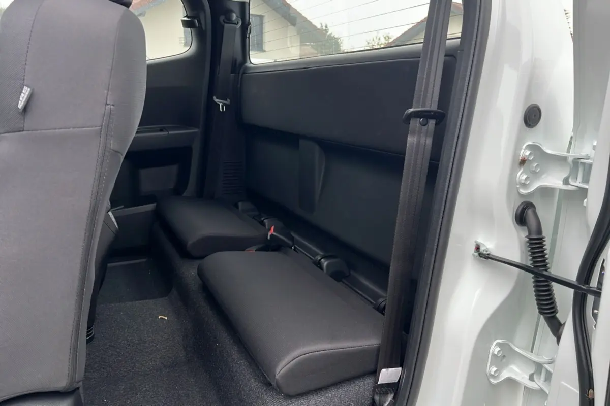 Vue intérieure arrière côté droit du pick-up Isuzu D-MAX Splash White 2026 avec sièges strapontins noirs et portière ouverte.