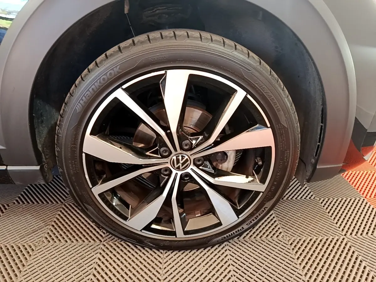 Gros plan sur la roue avant droite du Volkswagen Taigo noir 2023, mettant en valeur la jante alliage bicolore et le logo VW central.