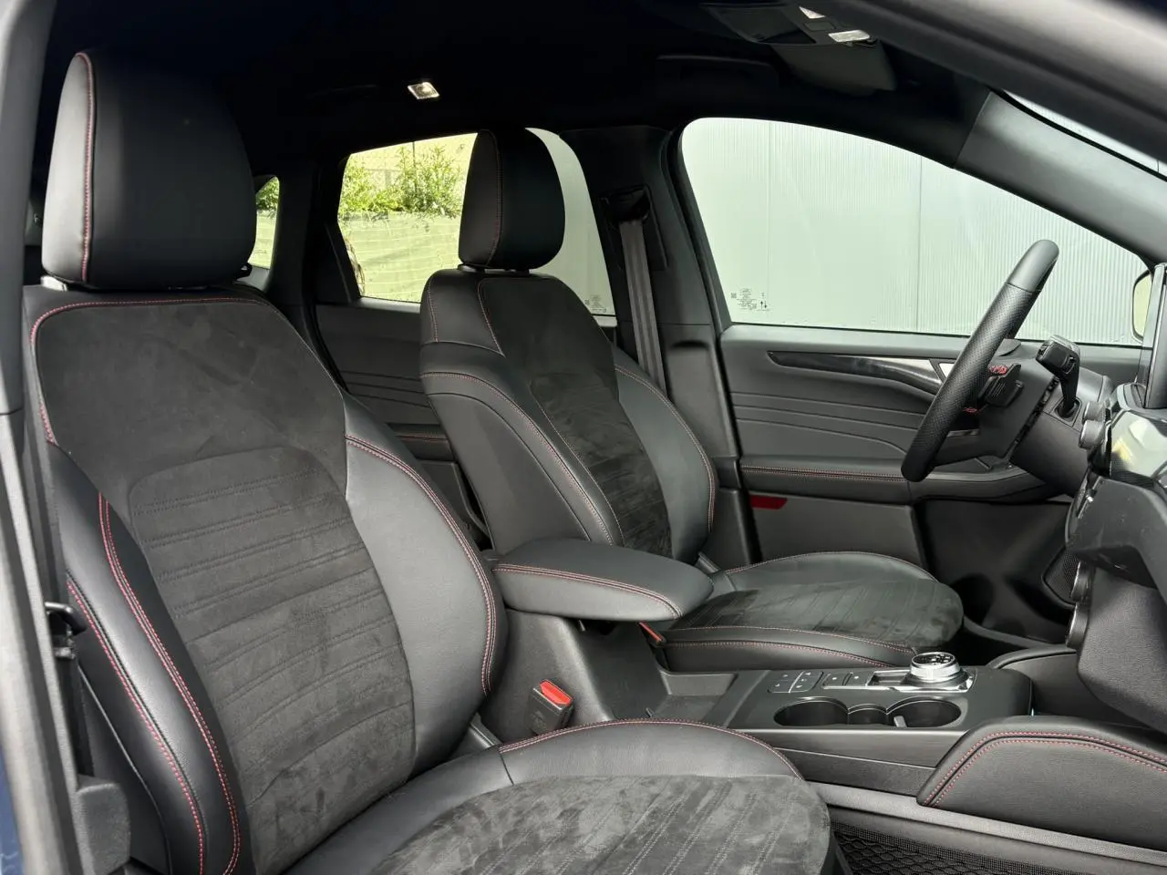 Vue intérieure côté droit du Ford Kuga ST-Line X 2023, sièges noirs avec surpiqûres rouges et volant méplat.