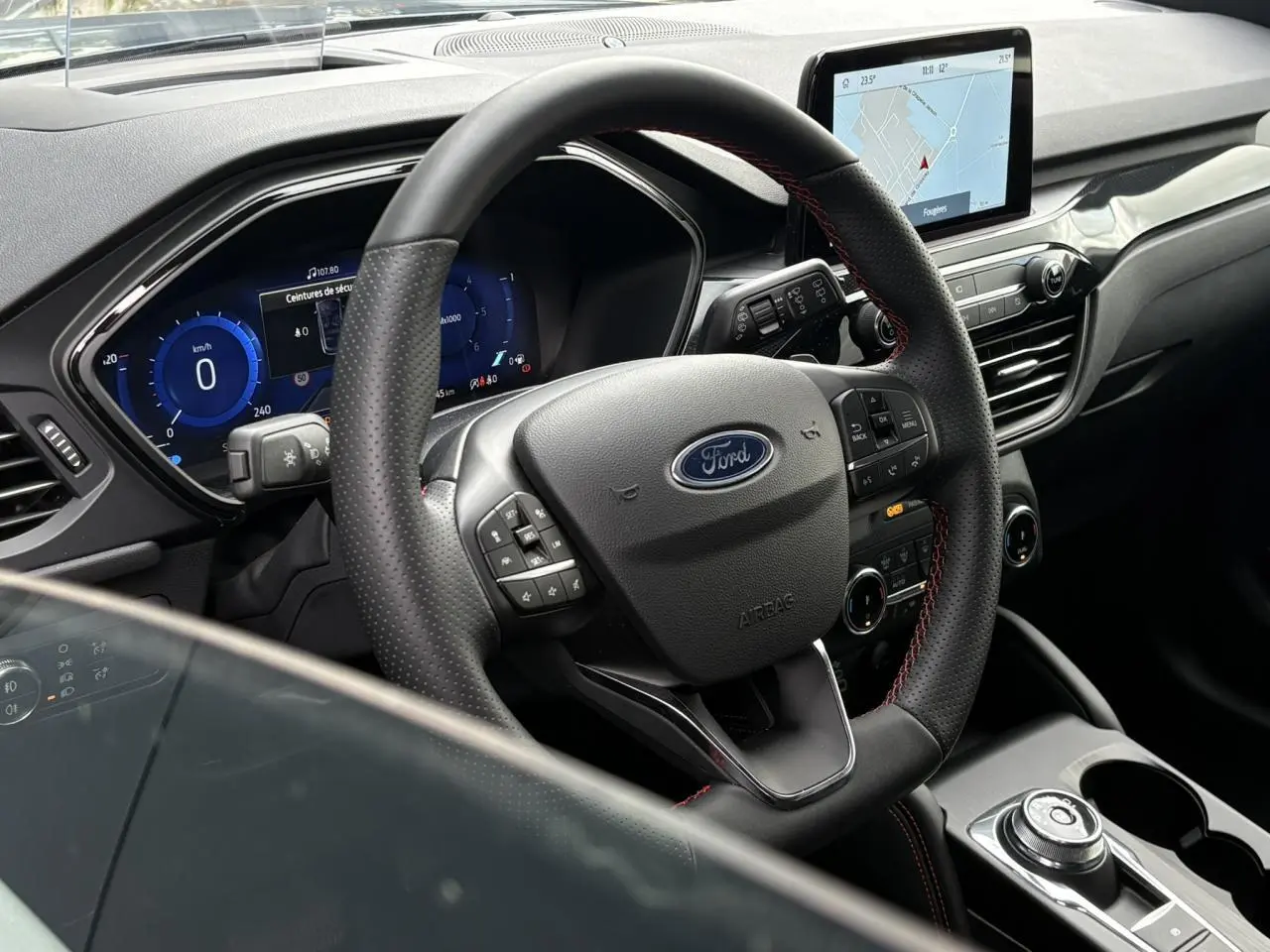 Vue intérieure centrée sur le volant noir perforé avec surpiqûres rouges et l’écran tactile du tableau de bord du Ford Kuga.