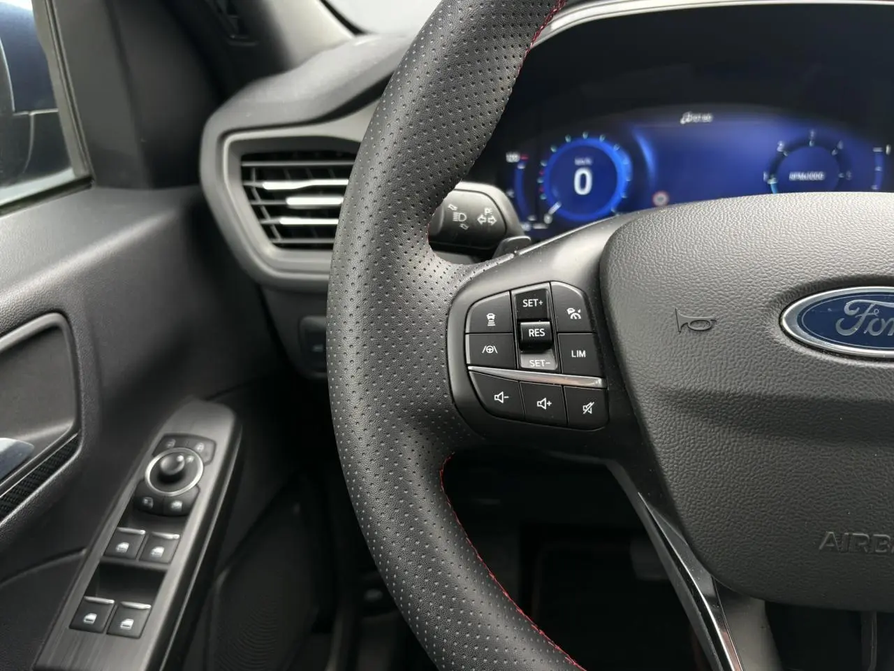 Vue rapprochée du volant perforé avec surpiqûres rouges et tableau de bord numérique bleu du Ford Kuga 2023.