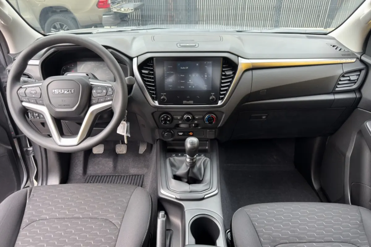 Vue intérieure avant de l'Isuzu D-MAX 2.2 TD 164 Space Evolution avec tableau de bord noir et levier de vitesses manuel.