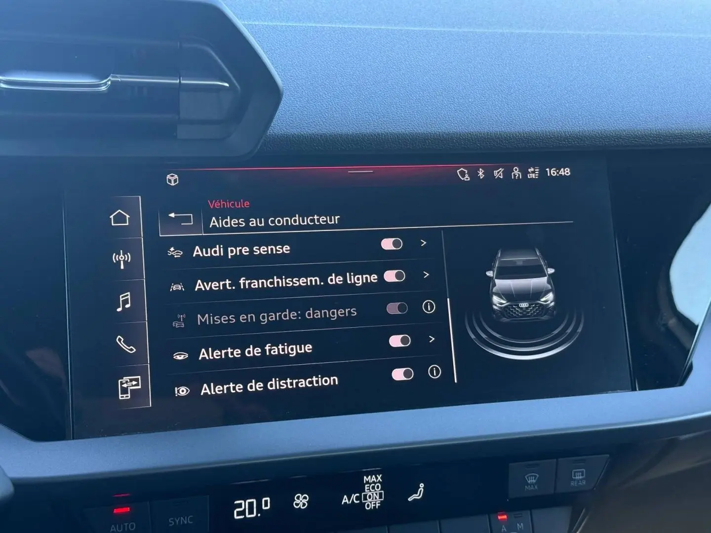 Écran tactile intérieur affichant les aides à la conduite d'une Audi A3 Sportback blanche, vue de face sur l'écran.