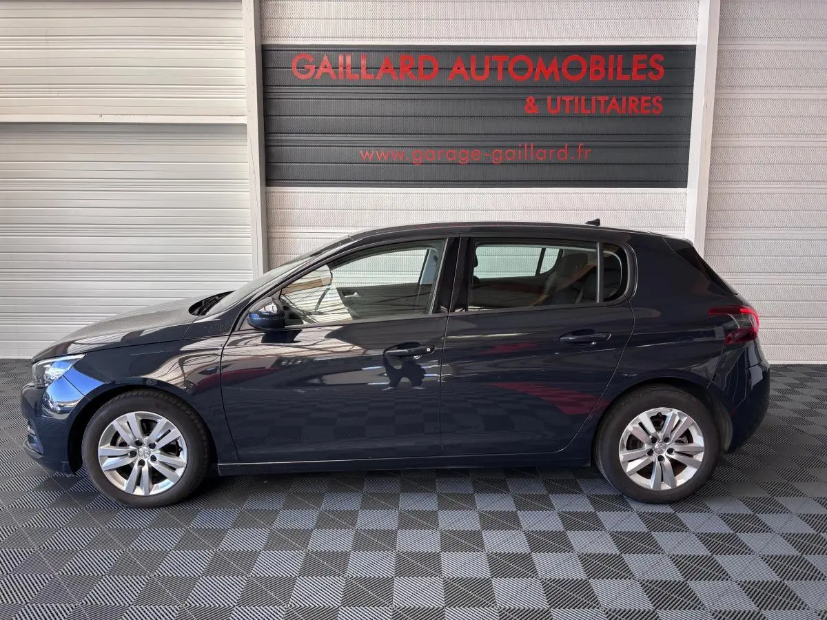 Profil côté gauche d'une Peugeot 308 gris foncé 2019 garée devant un mur avec logo Gaillard Automobiles.