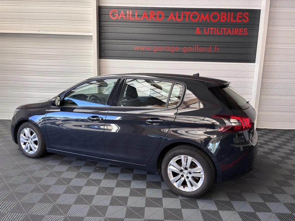 Peugeot 308 gris foncé vue de profil côté gauche dans un garage avec sol à damier noir et gris.