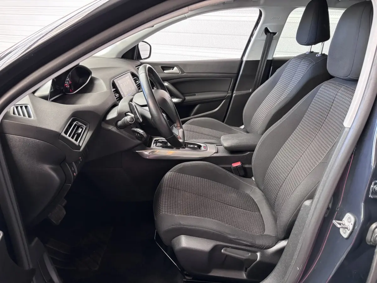 Intérieur avant droit d'une Peugeot 308 gris foncé, montrant sièges tissu, volant et console centrale moderne.