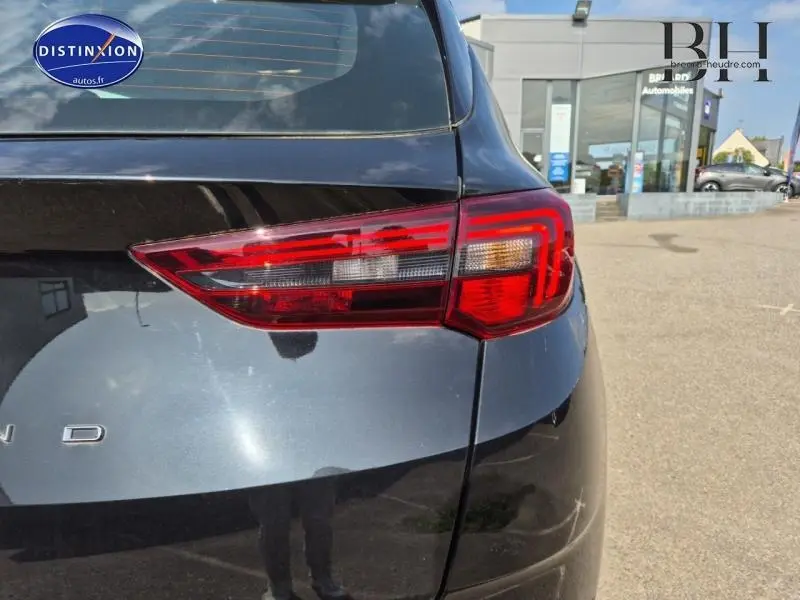 Gros plan sur le feu arrière droit d'un Opel Grandland noir Karbon métallisé, avec reflet du ciel et bâtiment en arrière-plan.