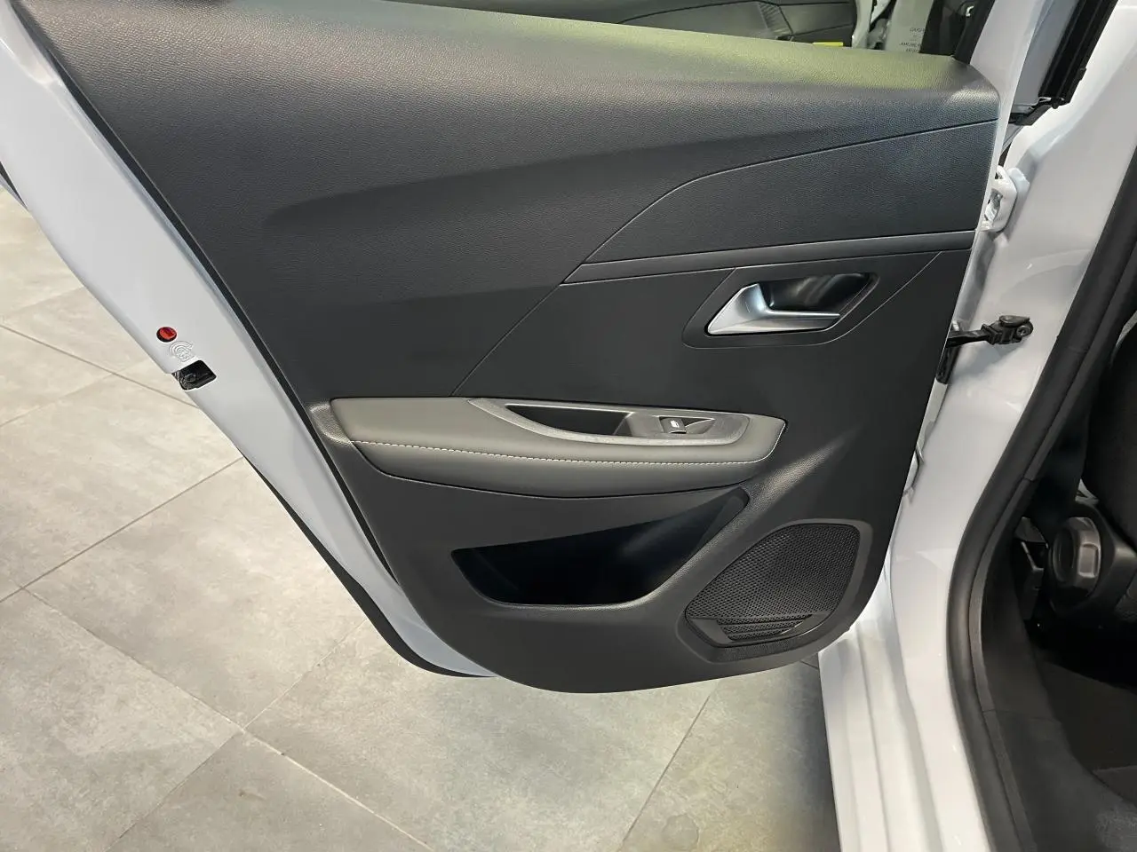 Vue rapprochée de la porte arrière gauche blanche okenite du Peugeot 208 1.2i Hybrid avec garniture noire et accoudoir gris clair.