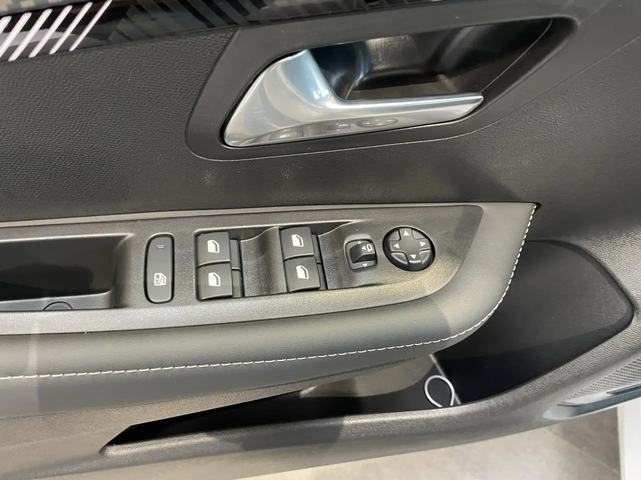 Gros plan sur la porte avant gauche de la Peugeot 208 blanche, montrant les commandes de vitres et le bouton de réglage des rétroviseurs.