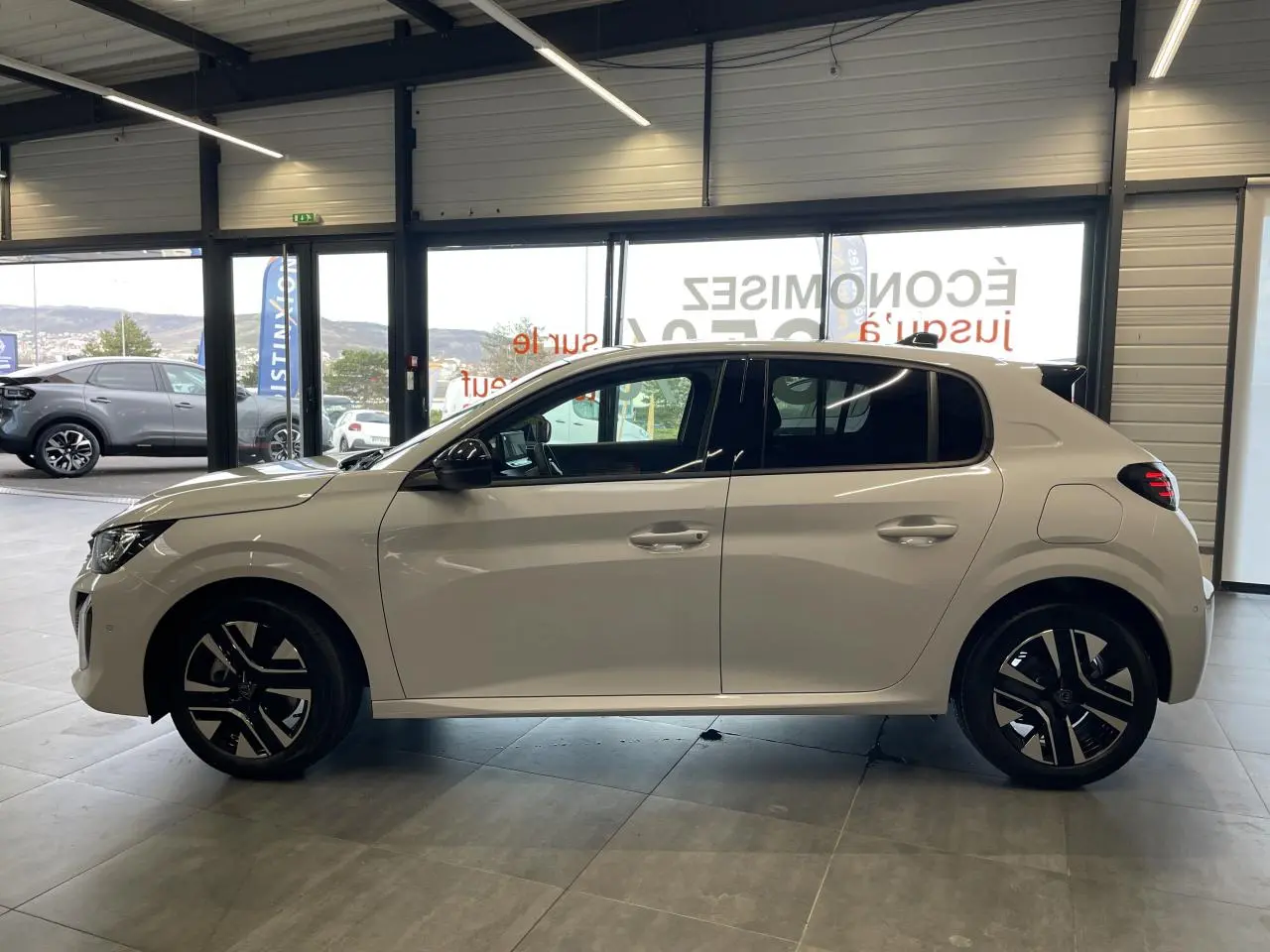 Peugeot 208 blanche vue de profil côté gauche, avec jantes alliage bi-tons et poignées couleur carrosserie.