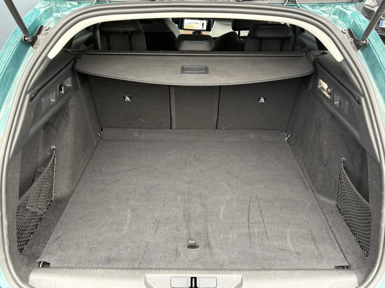 Coffre ouvert vu de l'arrière d'une Peugeot 308 SW Hybrid 145 bleu cuivre, avec filet de rangement latéral et cache-bagages.