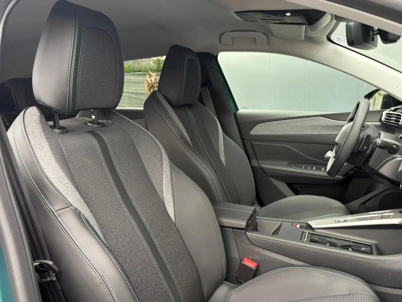 Vue intérieure côté avant droit du Peugeot 308 SW Hybrid 145 Allure, sièges tri matières gris avec surpiqûres bleues.