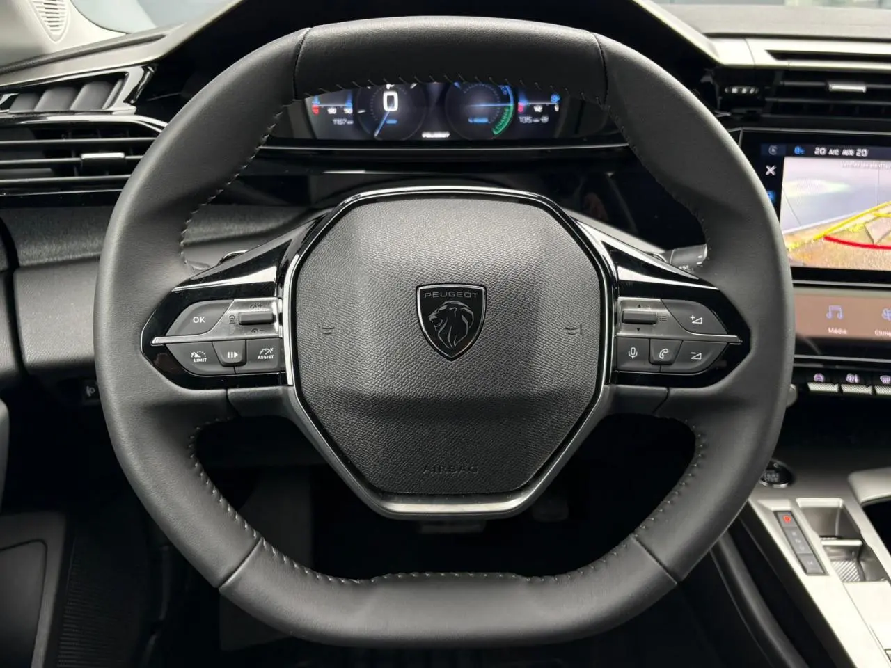 Vue rapprochée du volant cuir noir de la Peugeot 308 SW Hybrid 2025 avec commandes intégrées et tableau de bord numérique.