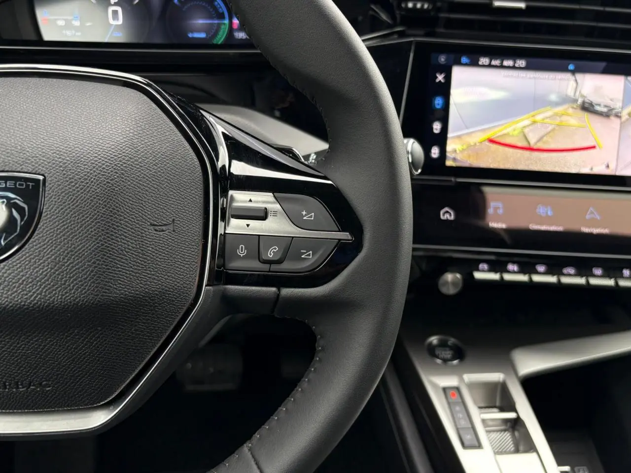 Vue rapprochée du volant noir de la Peugeot 308 SW Hybrid 2025 avec commandes intégrées et écran tactile affichant la caméra de recul.