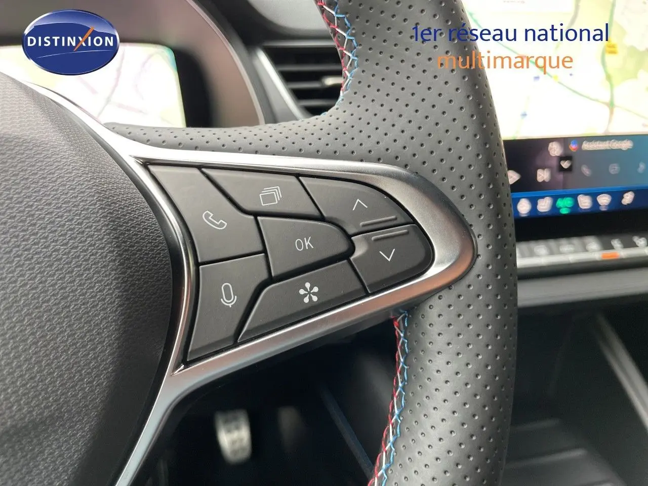 Gros plan sur les commandes à droite du volant perforé avec surpiqûres tricolores, écran tactile en arrière-plan.