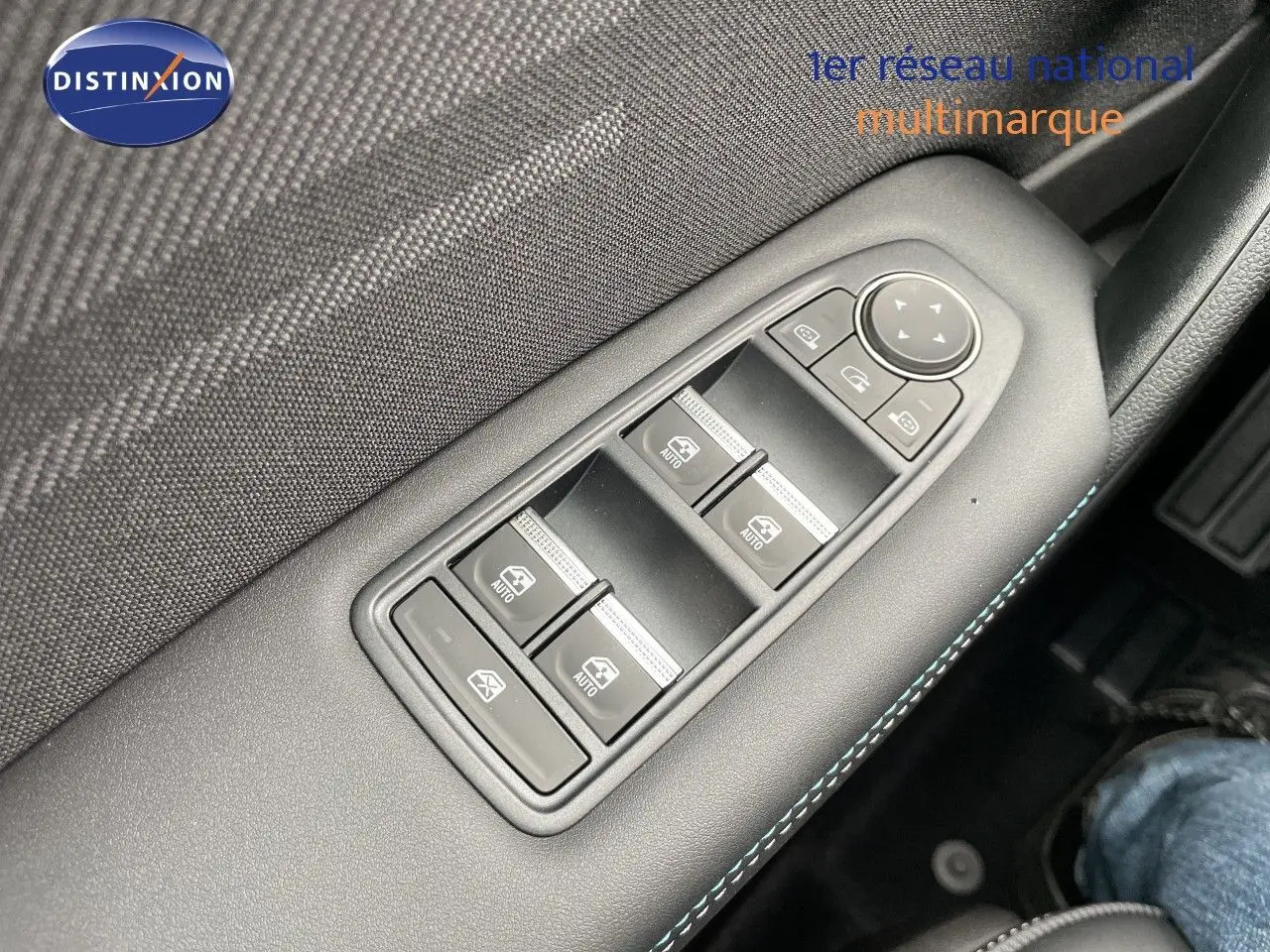 Gros plan sur les commandes des vitres électriques côté gauche d’un Renault Symbioz gris Rafale Métal, intérieur noir avec surpiqûres bleues.