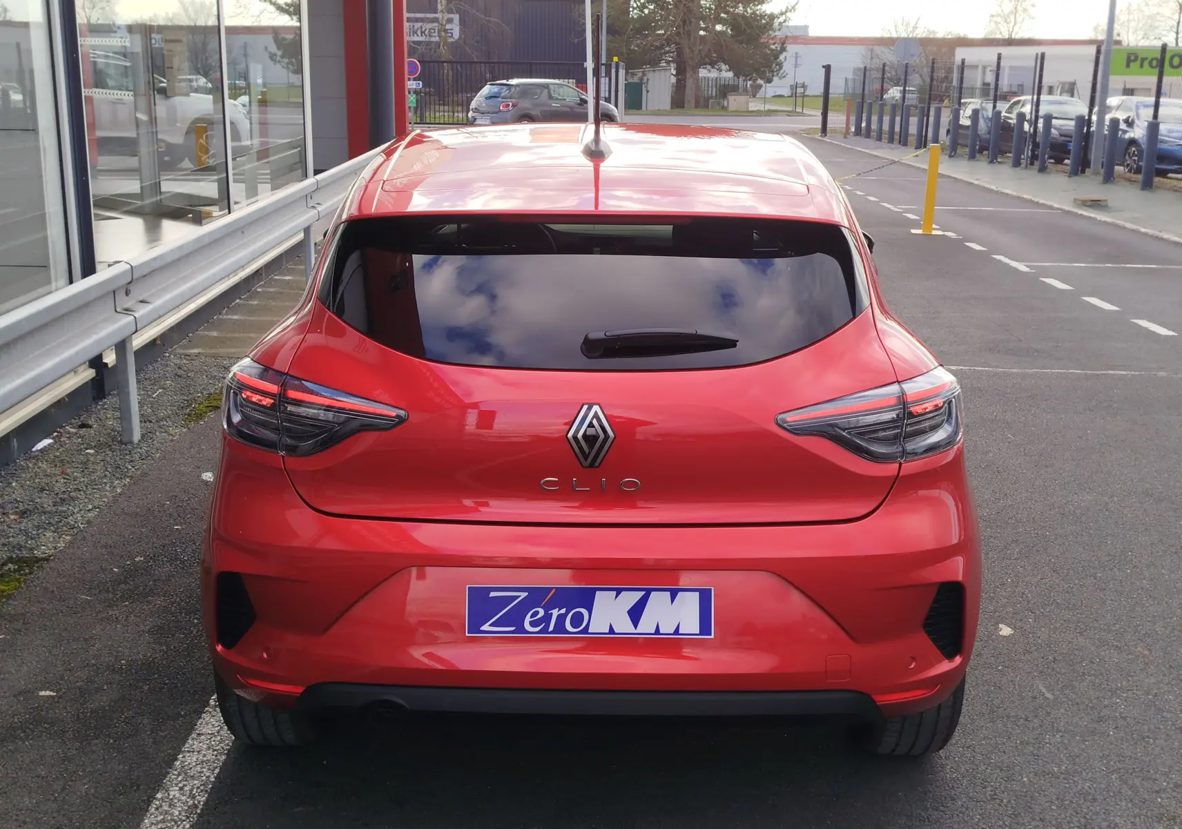 Vue arrière d'une Renault Clio rouge flamme 2025 avec feux LED et vitres arrière teintées sur parking urbain.