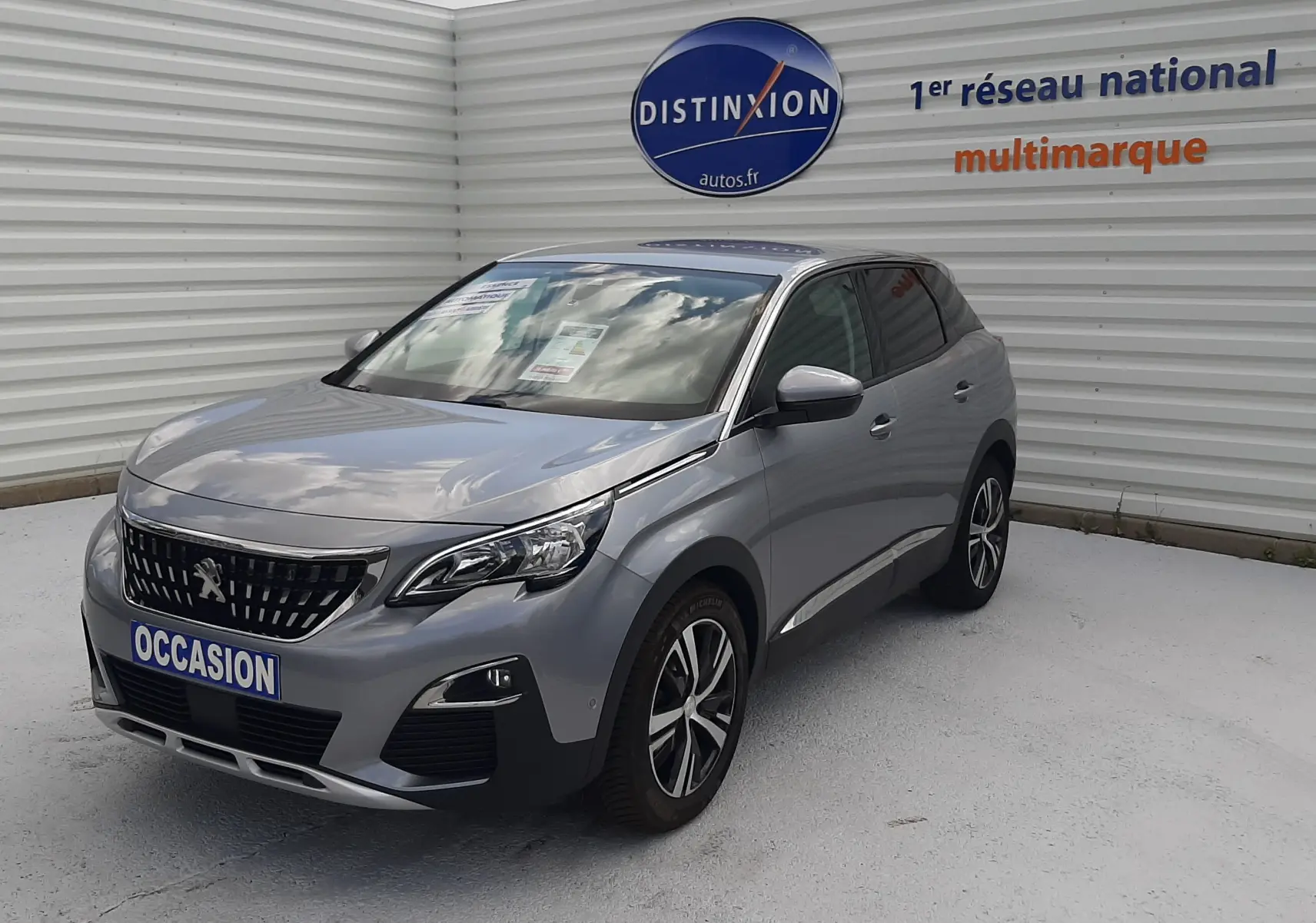 Peugeot 3008 gris vue 3/4 avant droit, avec calandre distinctive et jantes alliage bicolores.