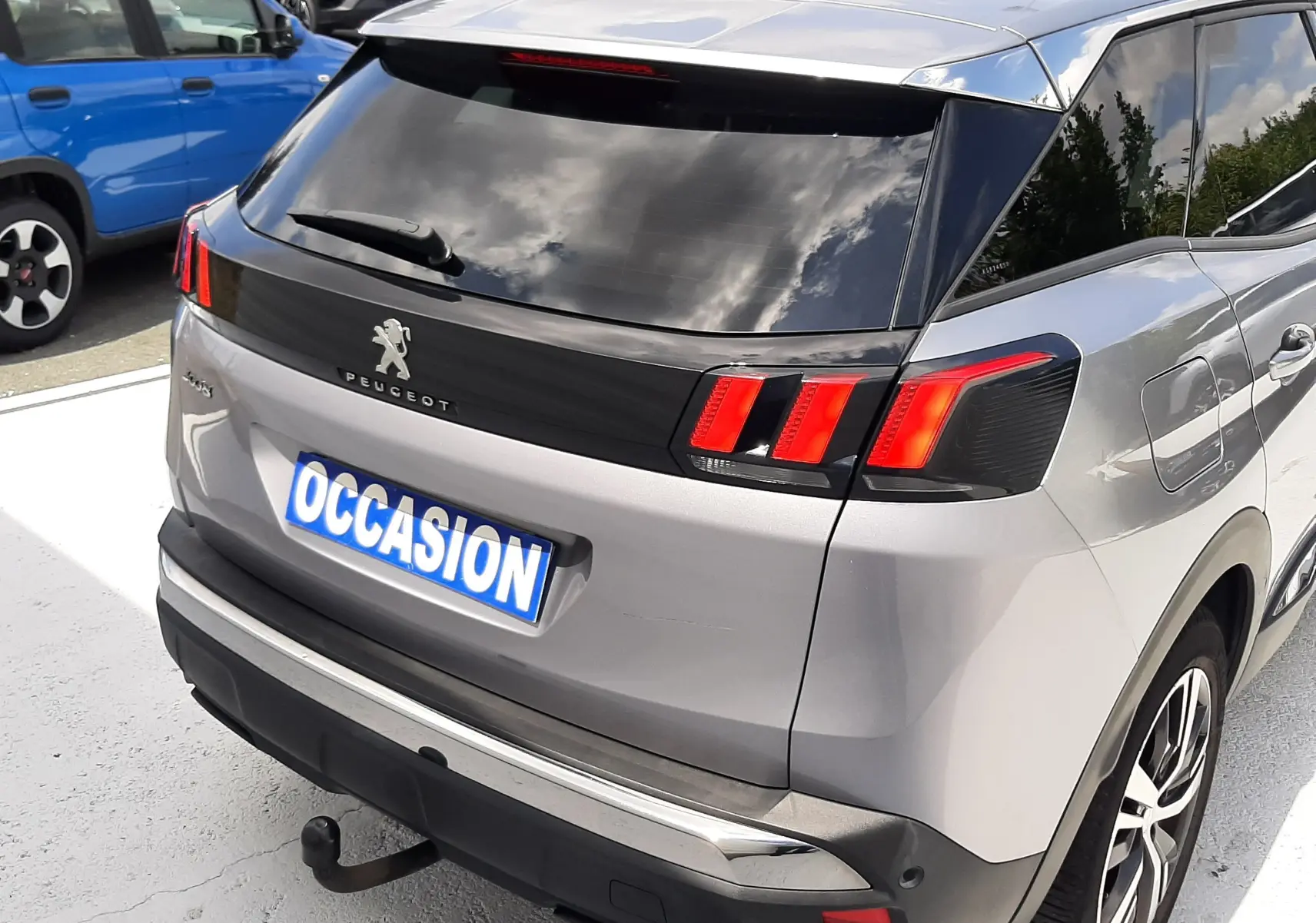 Vue 3/4 arrière droite d'un Peugeot 3008 gris 2020 avec feux arrière LED et attelage visible sur parking.