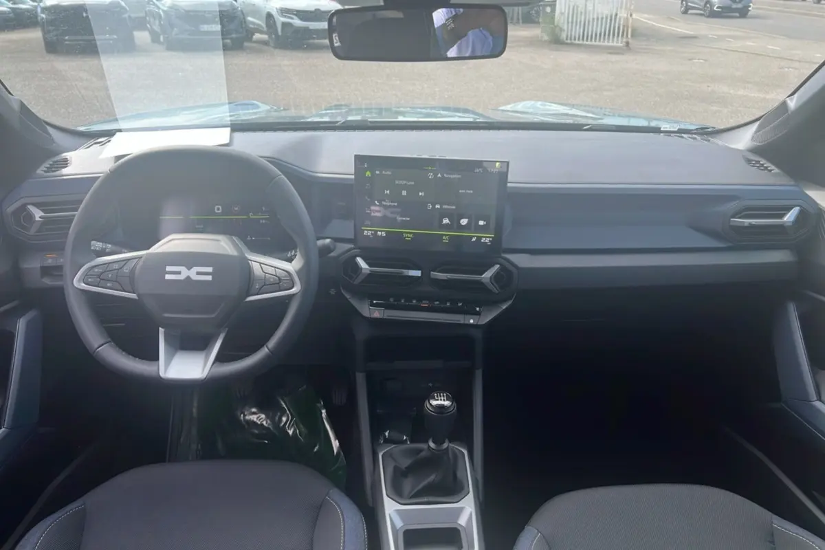 Vue intérieure frontale du tableau de bord du Dacia Bigster vert cèdre 2025 avec volant multifonction et écran tactile central.