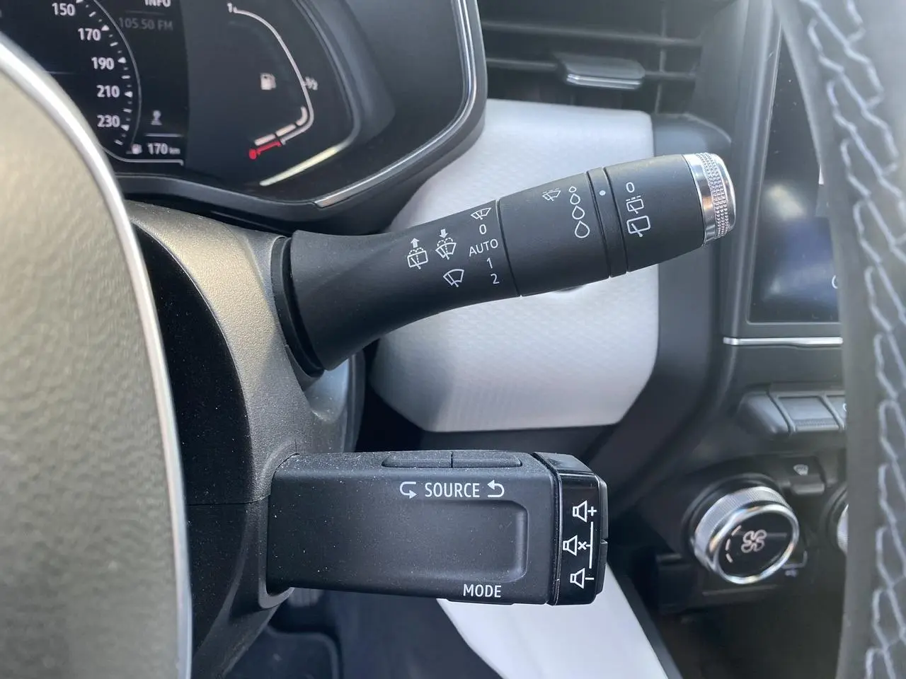 Détail des commandes au volant de la Renault Clio blanche 2021, avec commandes essuie-glaces et multimédia visibles.