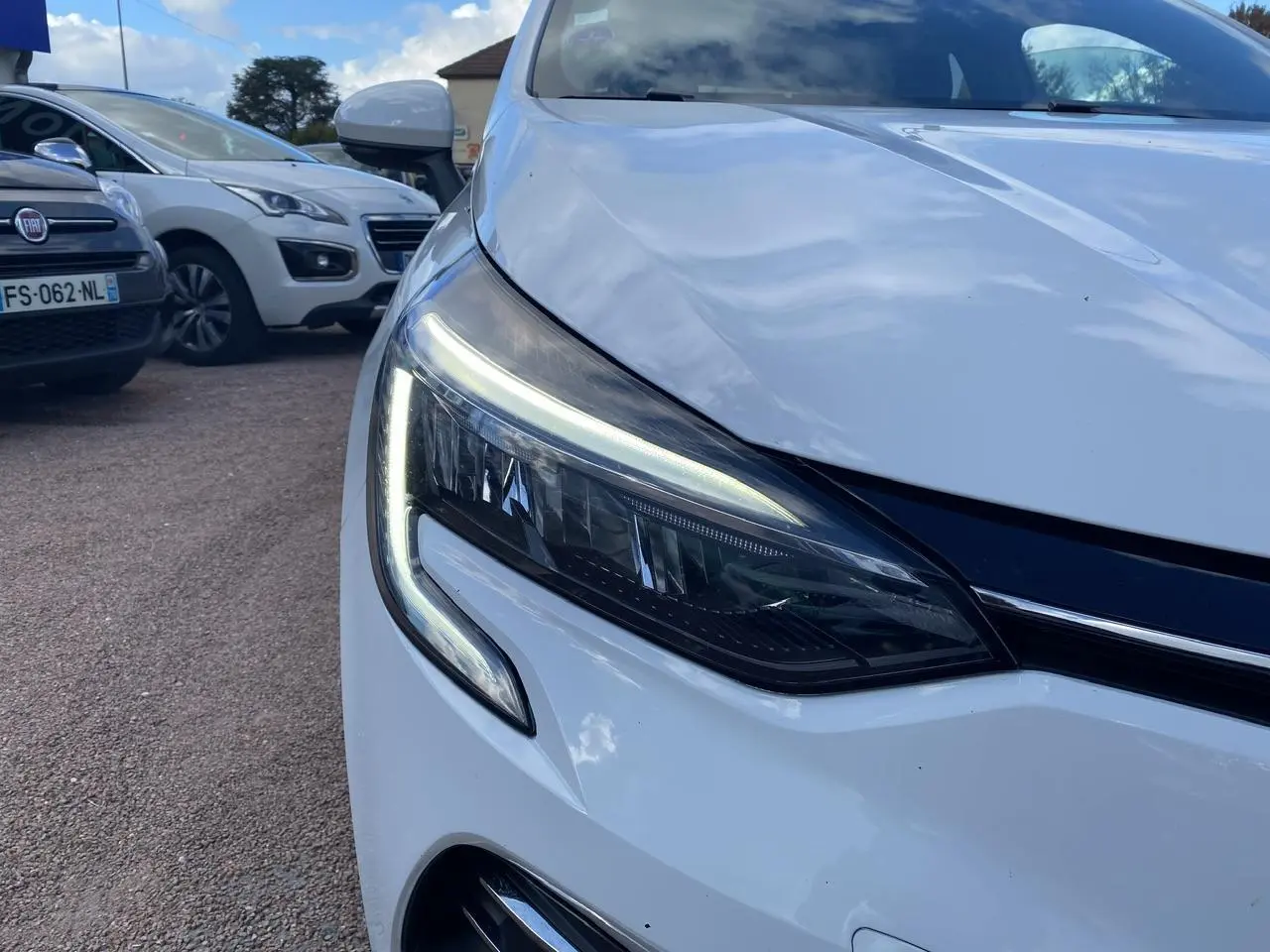 Gros plan sur le phare avant gauche LED d'une Renault Clio blanche 2021, soulignant son design moderne.