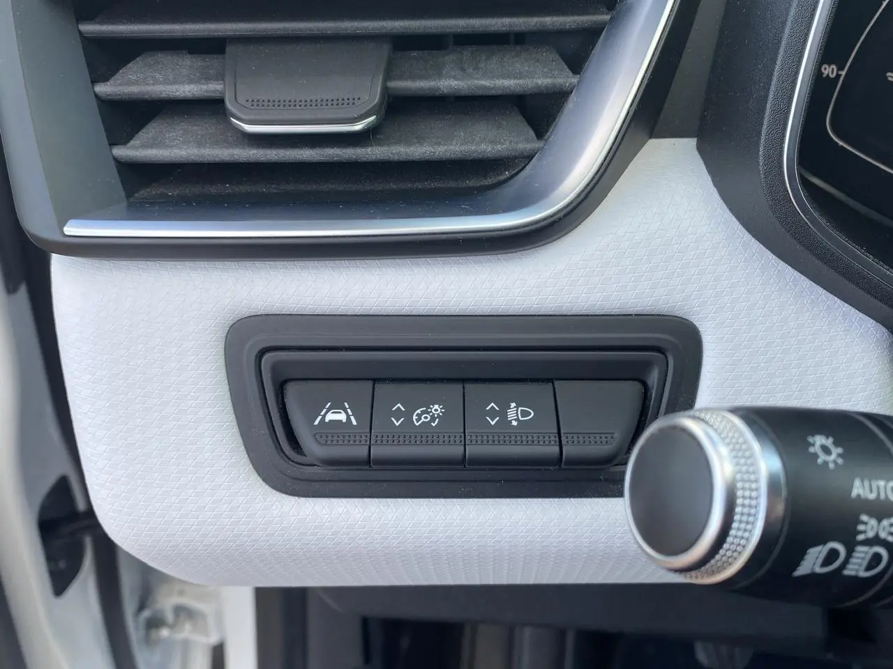 Gros plan sur les boutons de réglage d'aide à la conduite et éclairage dans l'habitacle blanc d'une Renault Clio 2021.