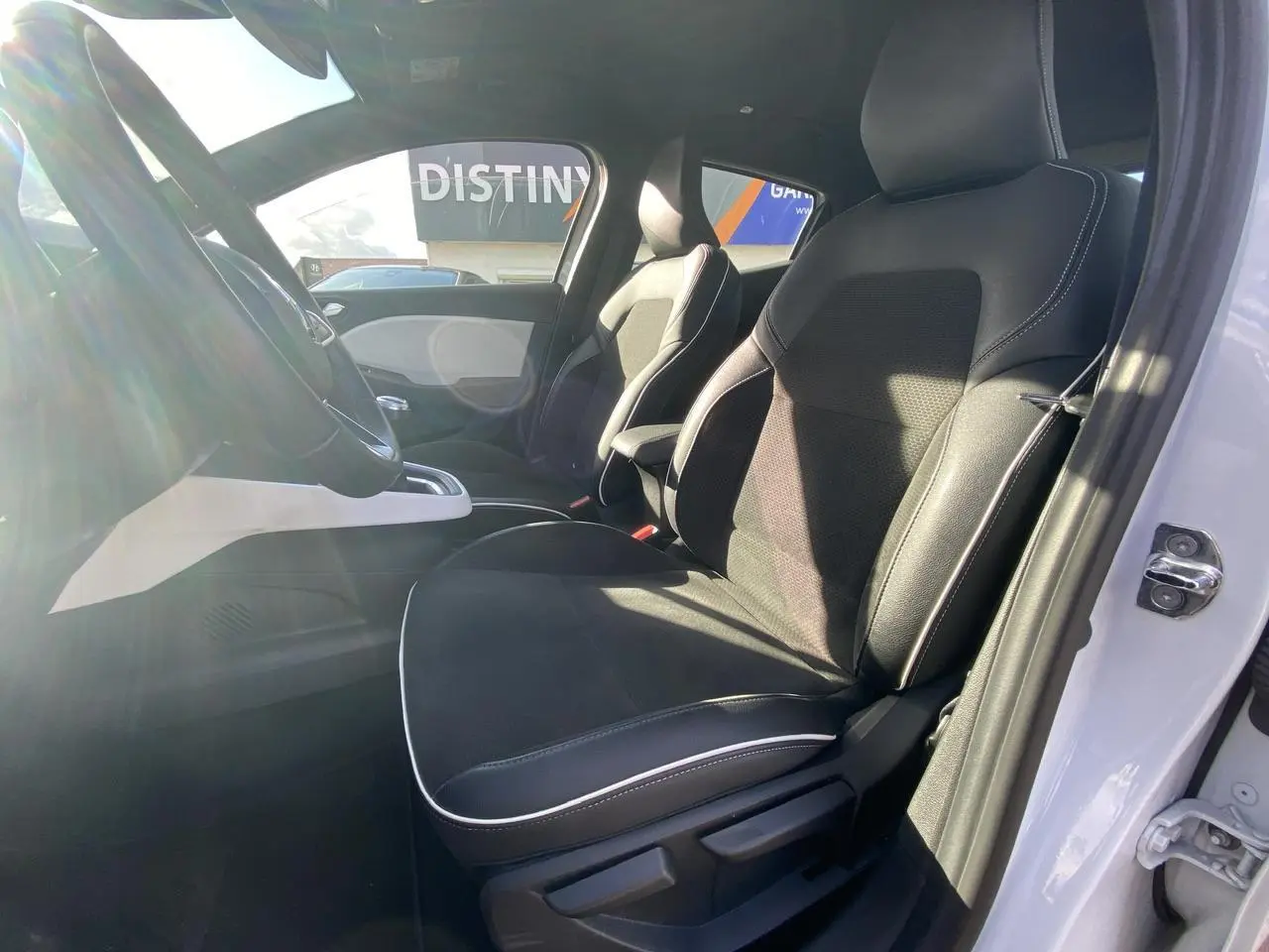 Intérieur de la Renault Clio blanc 2021 vu côté conducteur, sièges noirs en velours et cuir synthétique avec surpiqûres grises.